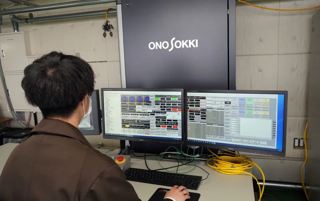 研究室で藤本教授がコンピュータモニターを使用して電気自動車の振動計測や制御に関する研究を行っている様子