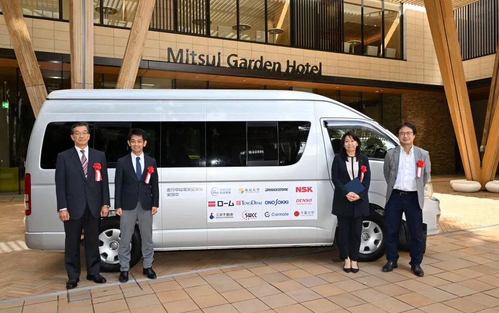走行中給電の公道実証実験出発式で、Mitsui Garden Hotelの前に停車した実証実験車両と、その前に立つ参加者たちの様子